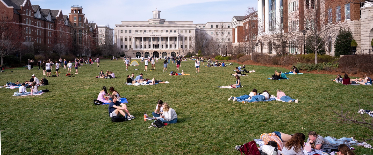 A photo with people outside sitting on the lawn in between buildings on campus