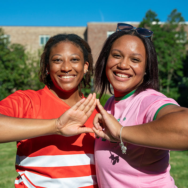 Two students making the sign of the sorority with their hands