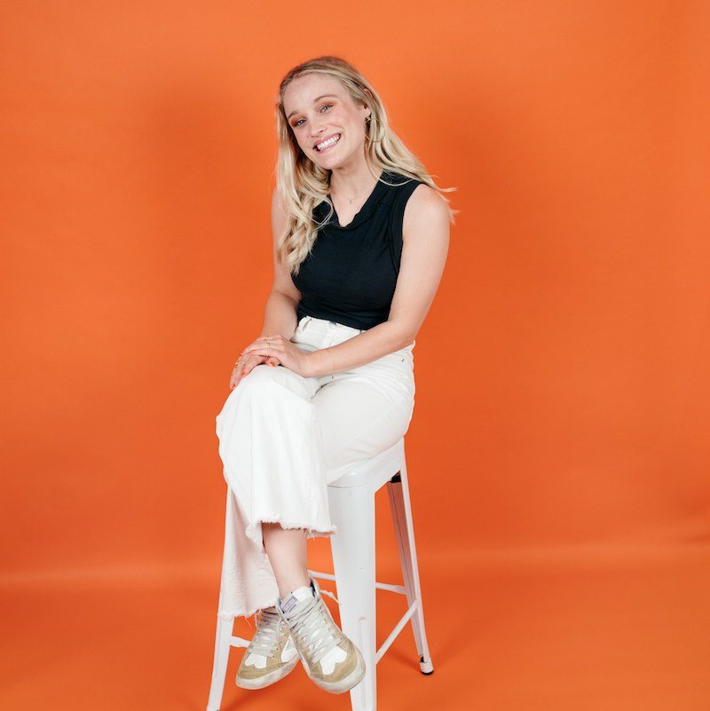 Abby Connolly sitting on a stool in front of an orange background