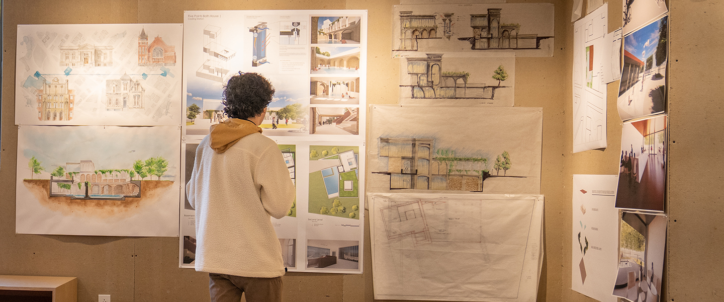 An O'More College of Architecture & Design student viewing architectural drawings that are hung on a wall