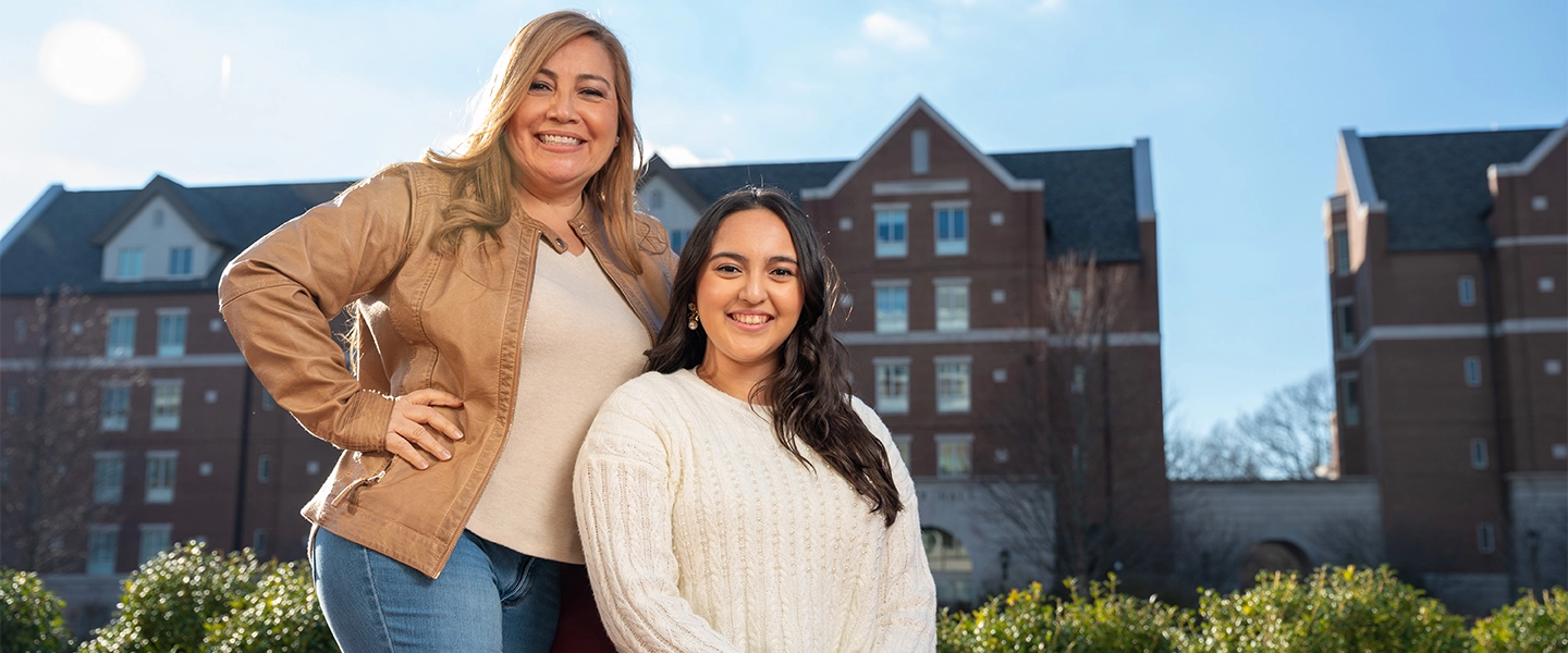 An outdoor photo of a mother and daughter with campus buildings in the background