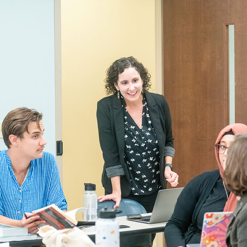 A professor smiling as she talks with a group of students in class