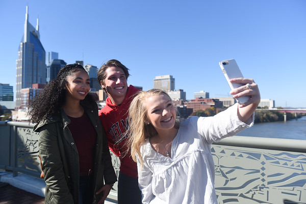 Students take a selfie on a bridge downtown, with the skyline on the horizon.