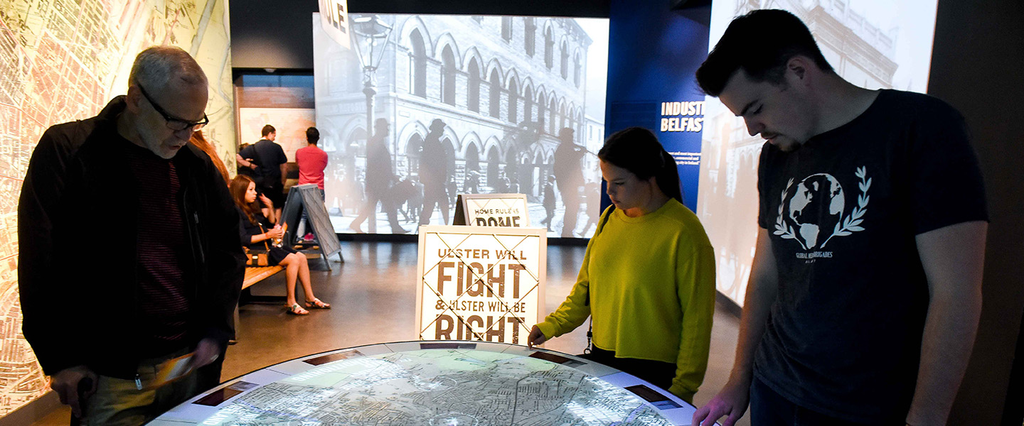 An indoor photo of people standing around an interactive map inside of a museum