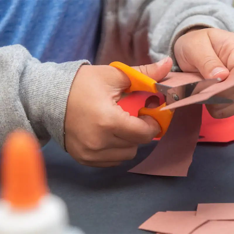 Child's hands using scissors to cut colored paper during an arts and crafts activity.