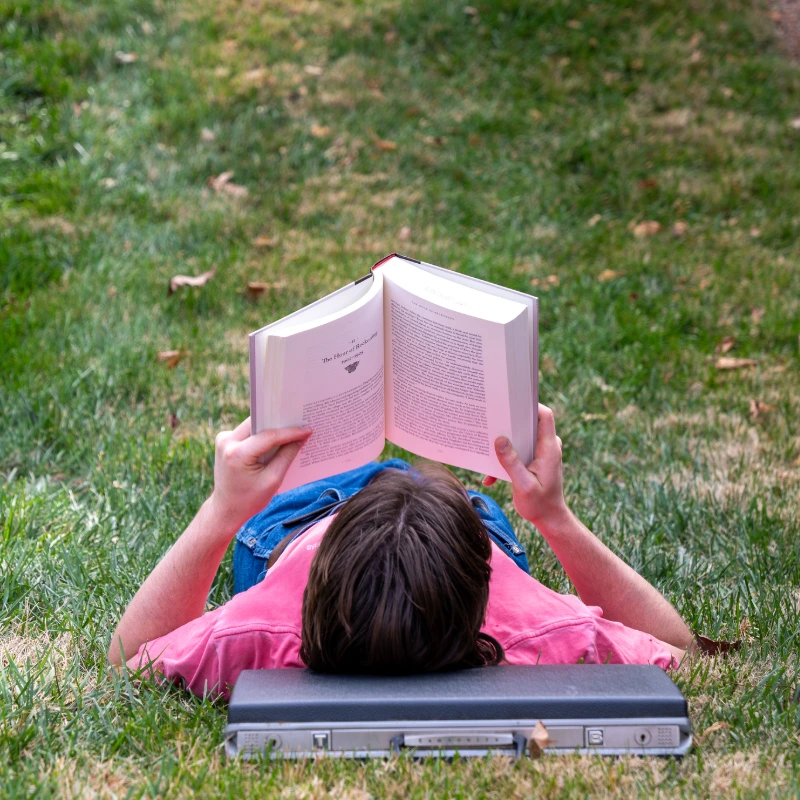 Two college students read a book while another works on a laptop.