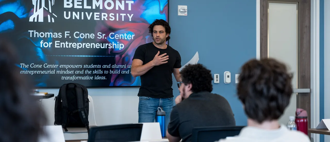Presenter speaks to a classroom of students in front of a Belmont University Thomas F. Cone Sr. Center for Entrepreneurship display.