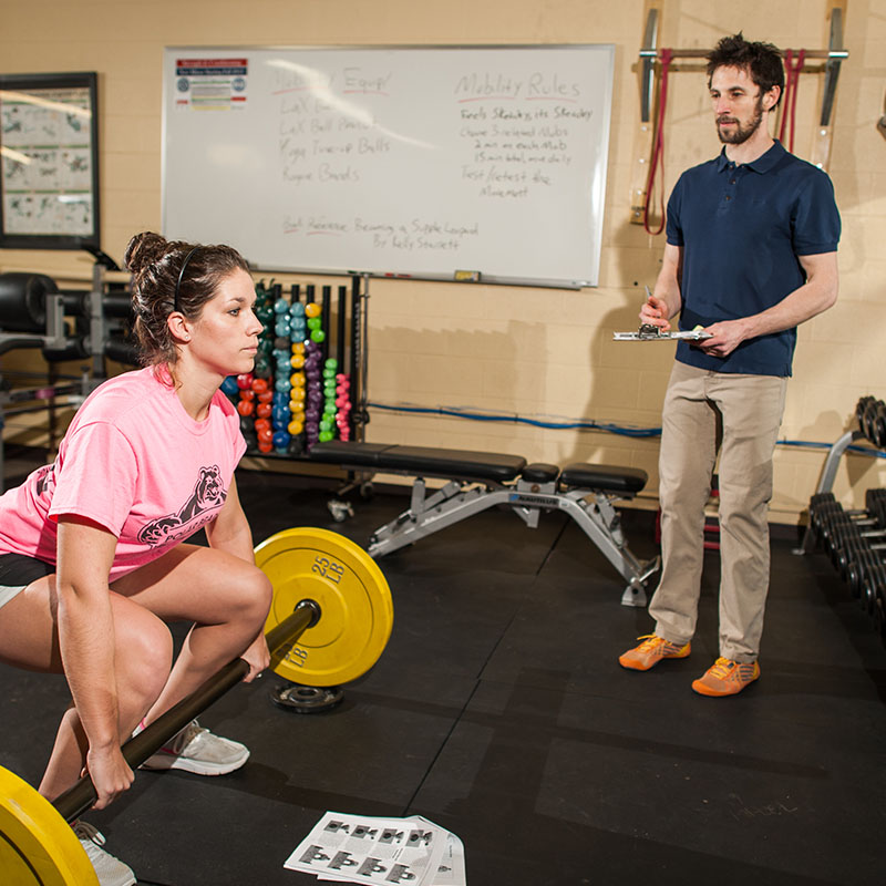 Exercise science student lifts weights while a professor measures their performance