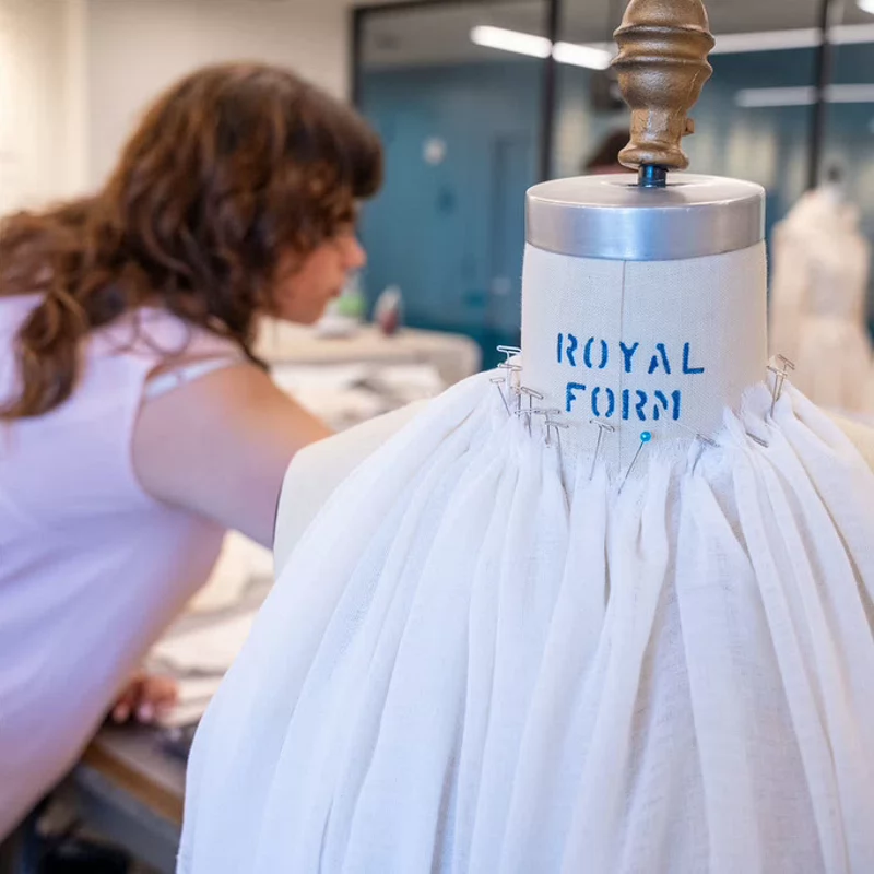 Fashion student drapes fabric on a dress form while working in a campus design studio.