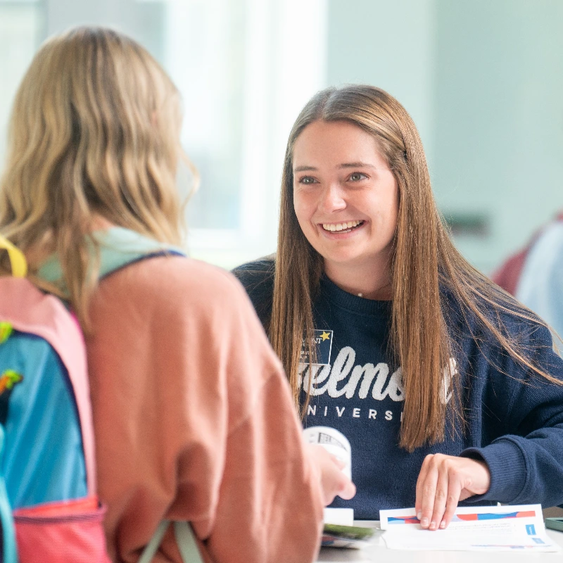 Smiling Belmont University student helps another student at an information desk.