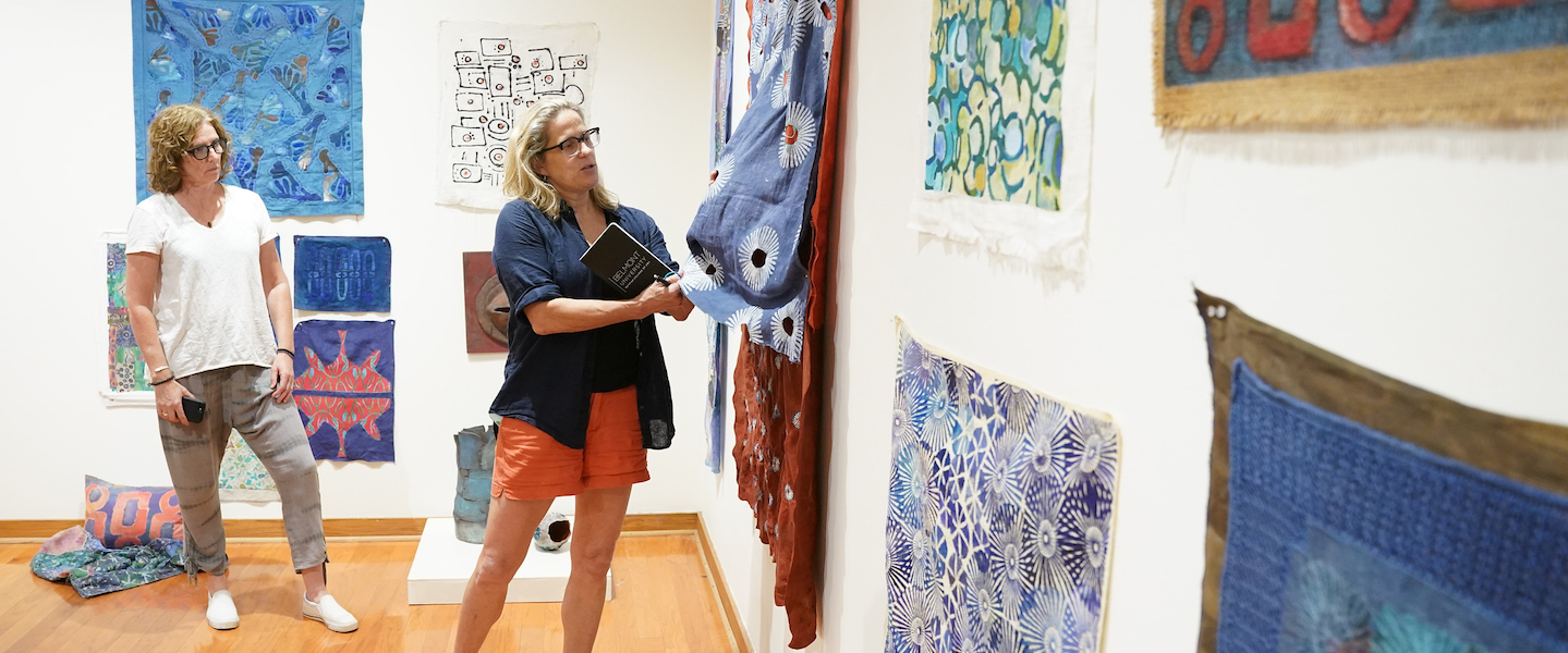 Two people looking at tapestries hung on the wall of a gallery