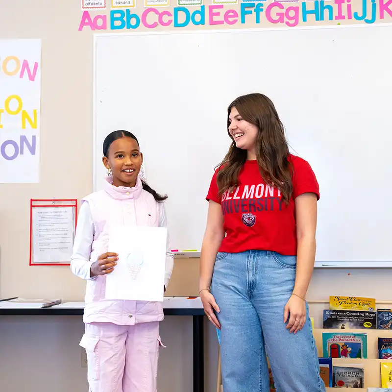 A Belmont teacher candidate supports a middle school student during a classroom activity, highlighting hands-on teaching experience and student engagement.