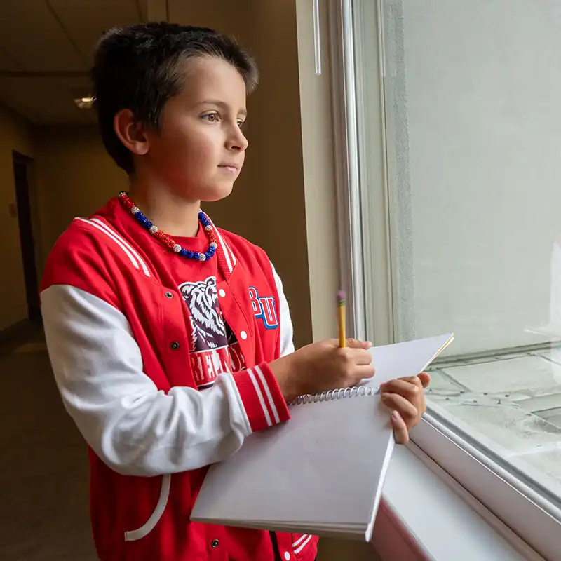 A middle school student taking notes/drawing while looking out of window