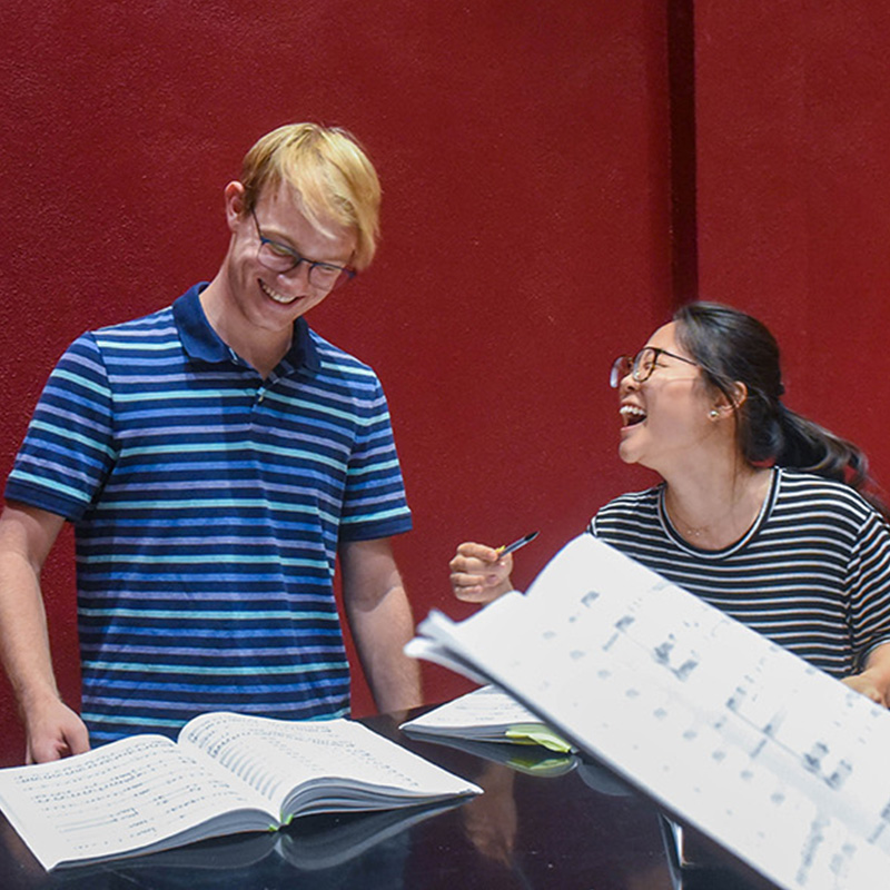 Two student laughing while standing at piano