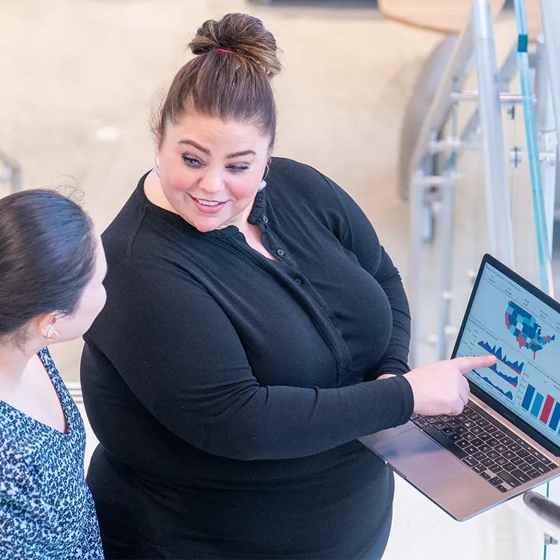 A mentor explains data visualizations on a laptop to a student, highlighting trends and insights.