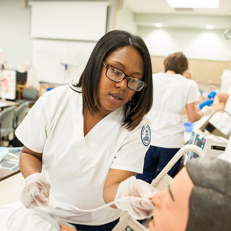 A nursing student inserting a tube into a patient simulator's nose