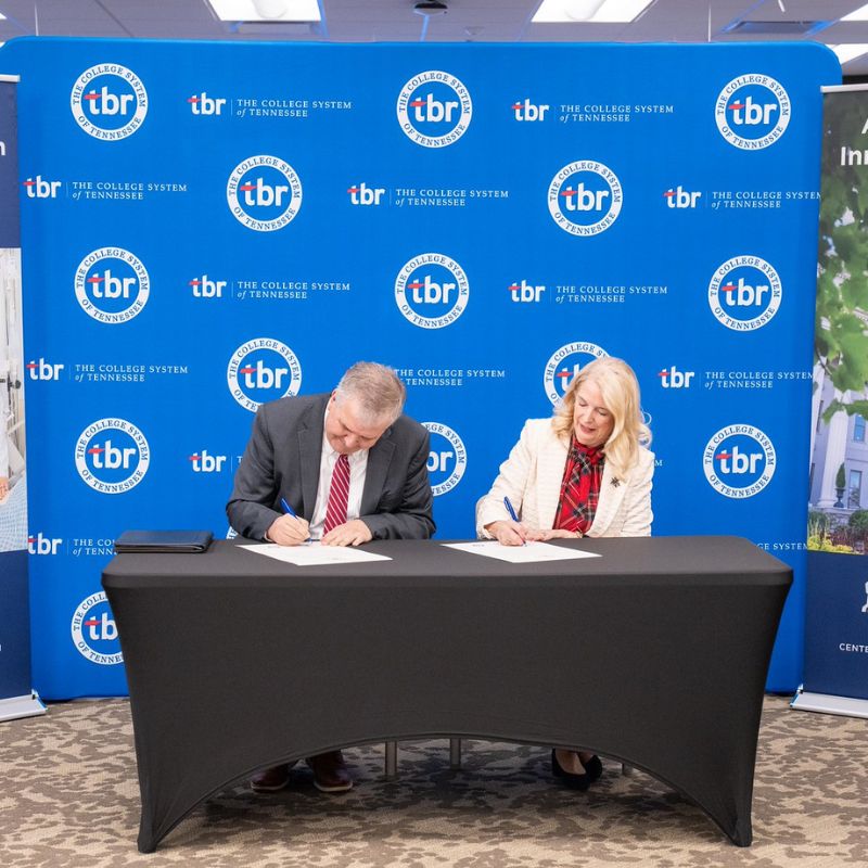 President Dr. Greg Jones and Tennessee Board of Regents (TBR) Chancellor Dr. Flora W. Tydings sign documents at a table during a formal agreement ceremony, with The College System of Tennessee (TBR) branded backdrop behind them.