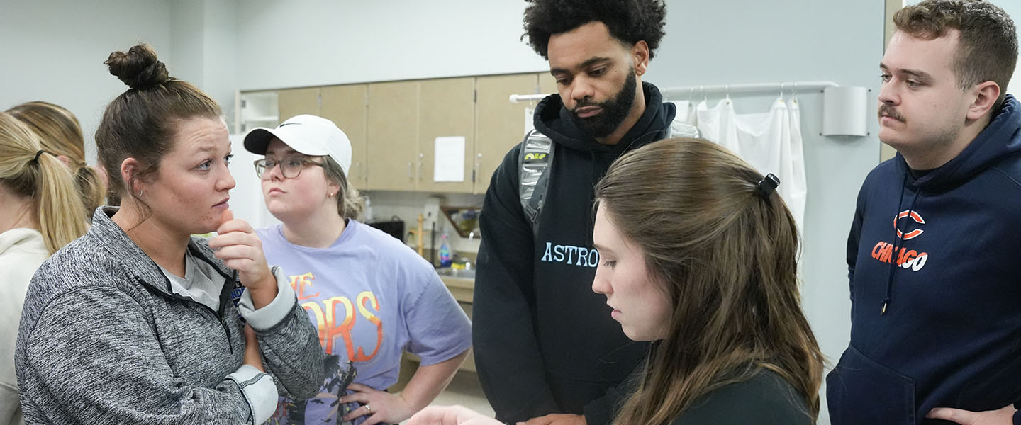 Four OT students discussing the layout of a room during a lab exercise