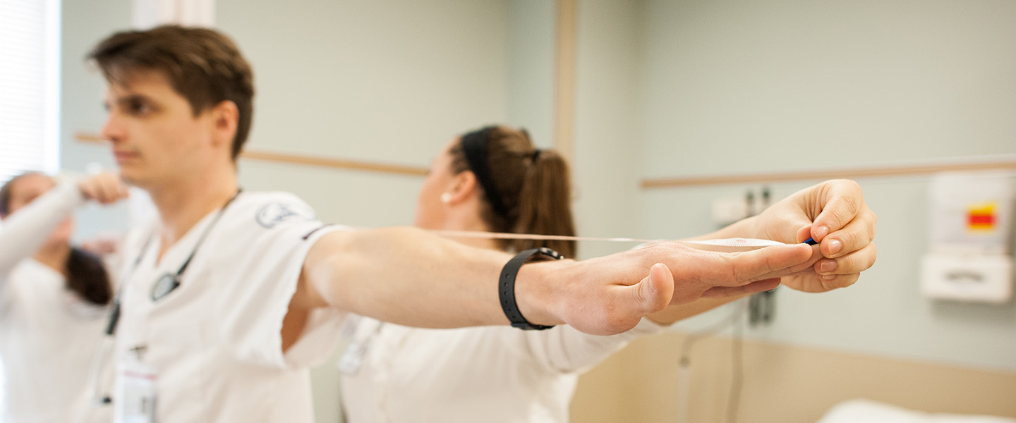 One physical therapy student measures the wingspan of another student.