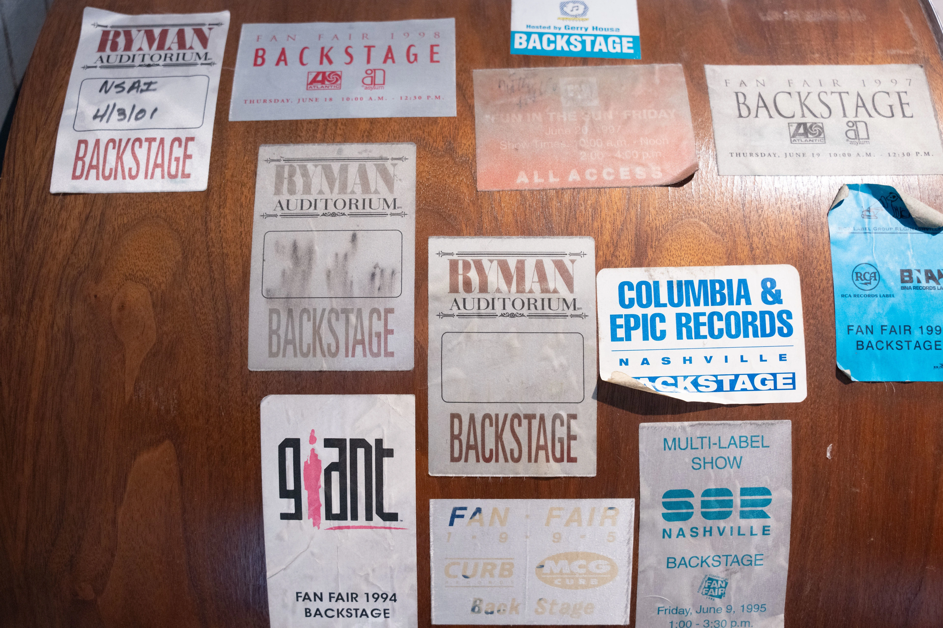 A collection of vintage backstage passes from various music events adorns a wooden surface, featuring diverse designs and logos, evoking nostalgia.