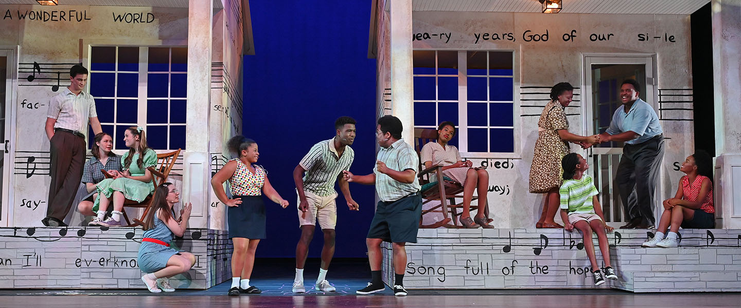 A group of students perform in front of a set on stage.