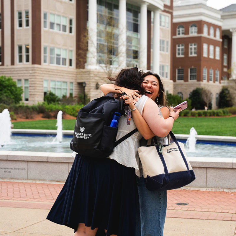Two female Belmont students embracing in a hug by the campus fountains
