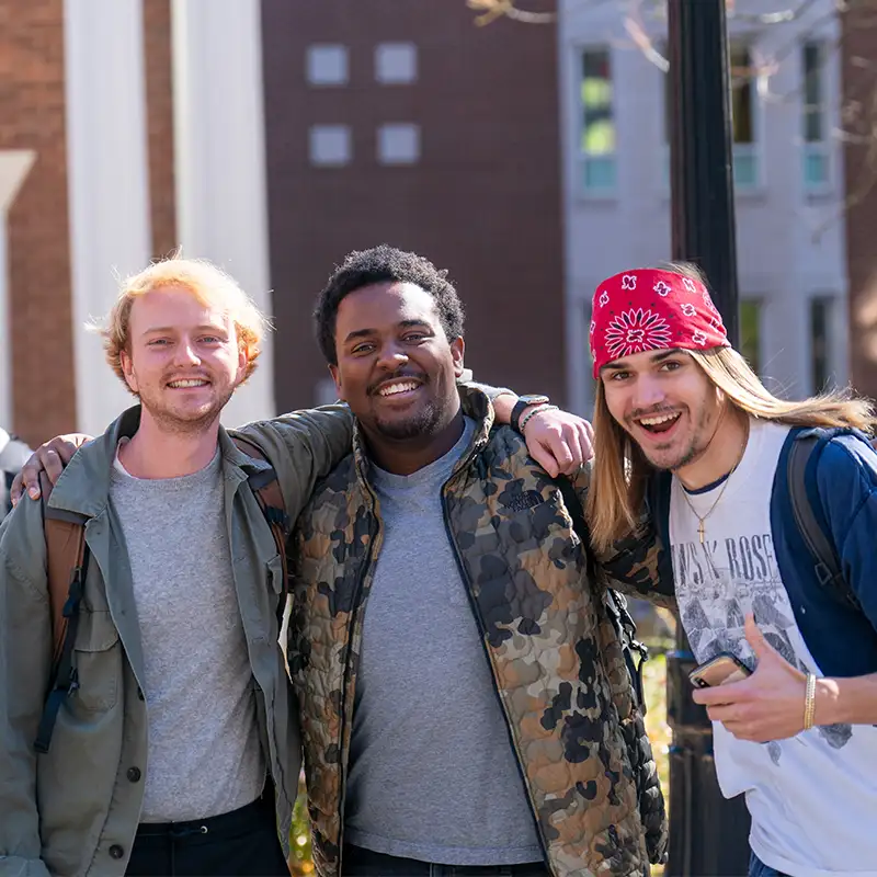 A diverse group of three male students in an embrace