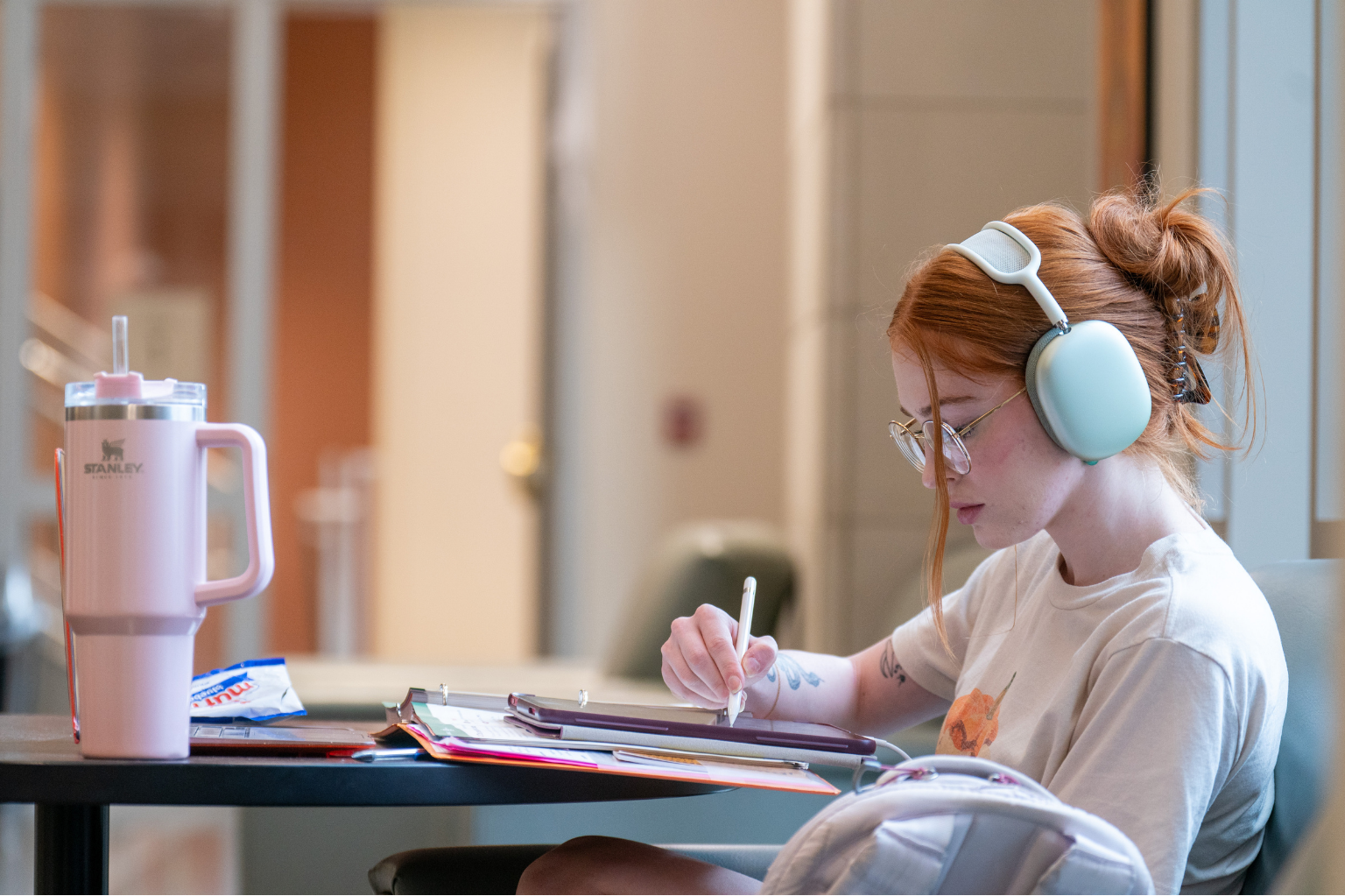 Female student sits at a table with headphones on, working on her iPad