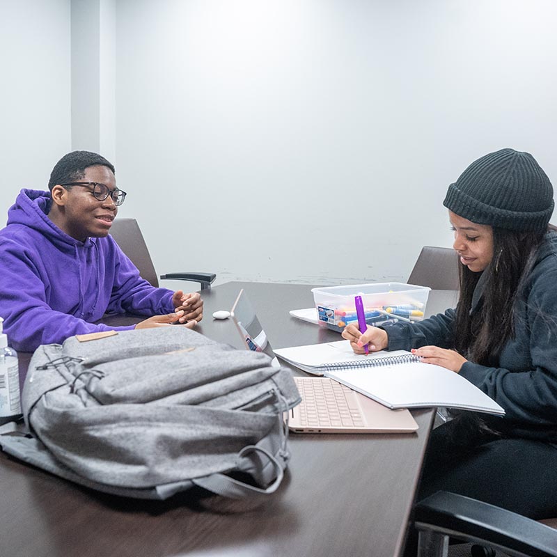 2 students sit at study table and take notes on school work assignment