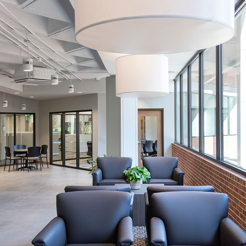 An interior view of a Belmont Central with comfortable chairs, large windows, and contemporary lighting.