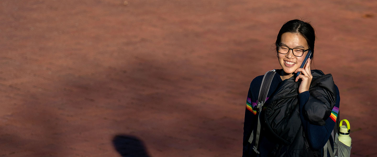 A student walking across campus talking on a phone