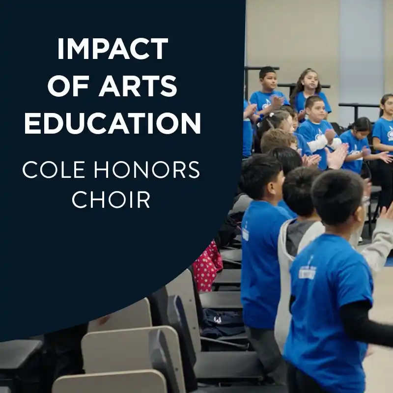 Instructor claps while leading a group of young students in blue shirts during choir rehearsal in a classroom with risers, piano, and music stands, with the text "Impact Of Arts Education Cole Honors Choir".