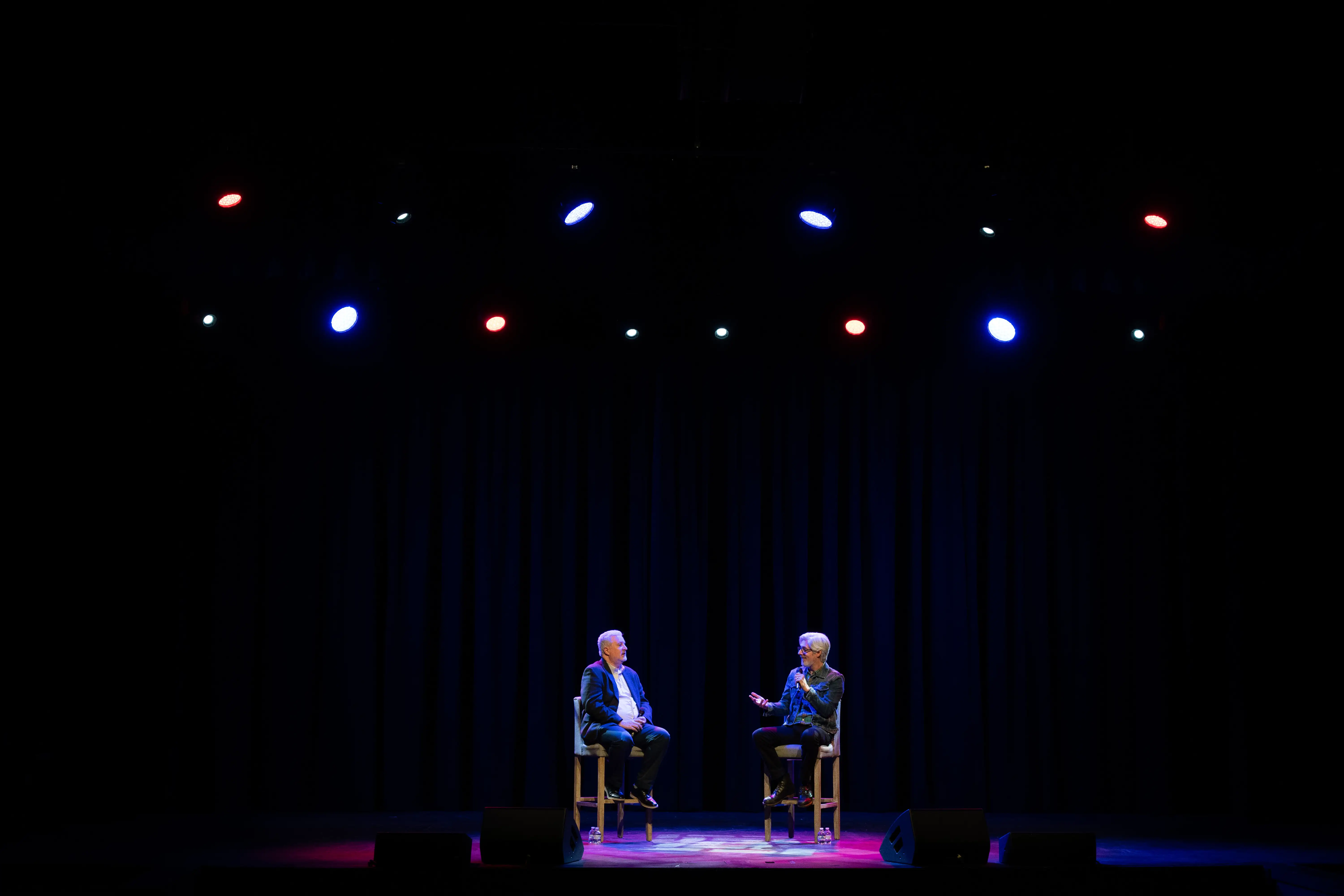Matt Maher and interviewer sit on stools having a conversation under red, white, and blue spotlights onstage in Massey Concert Hall during a master class event.