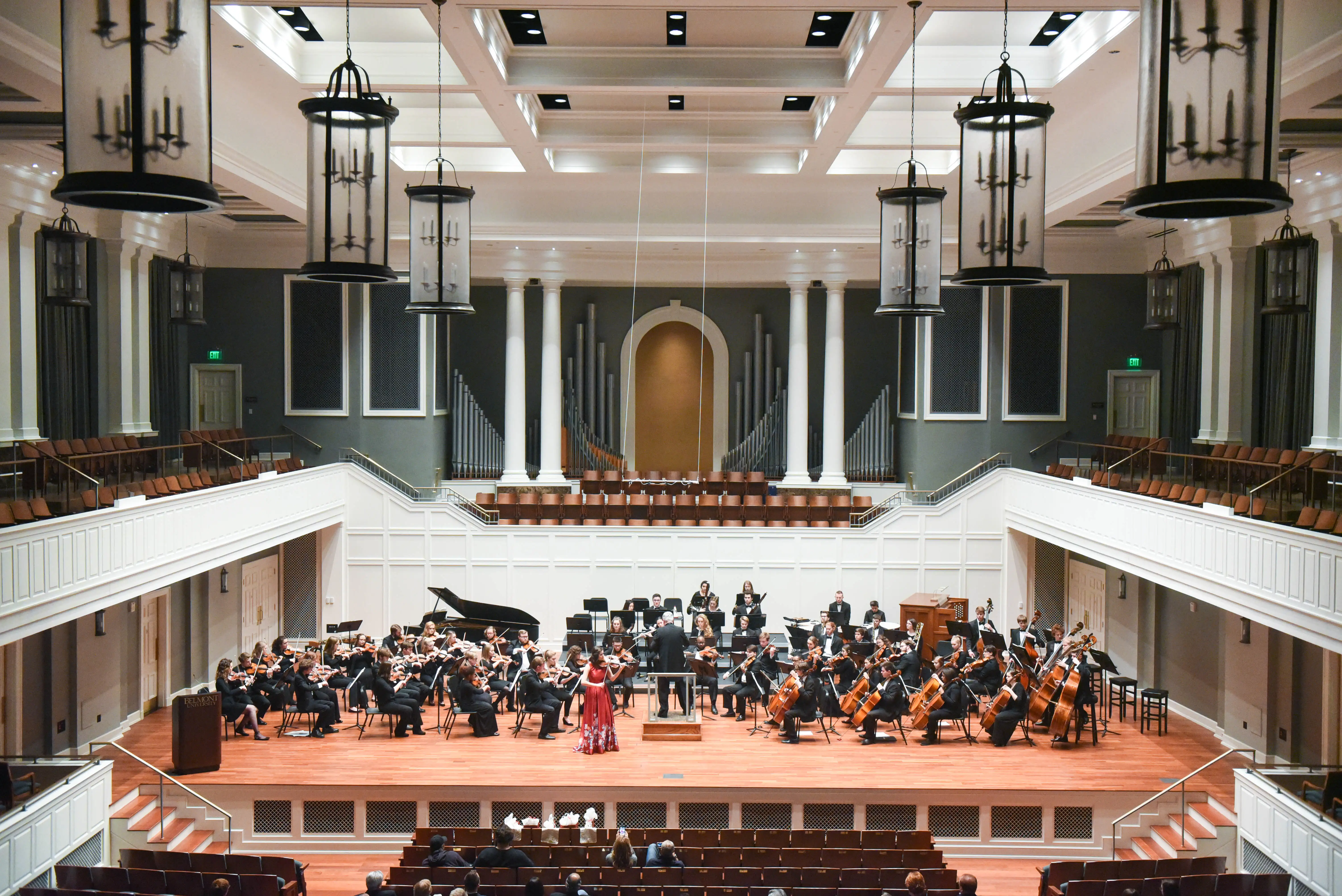 Orchestra and vocal soloists perform onstage in McAfee Concert Hall, surrounded by white columns and an audience-filled concert space.