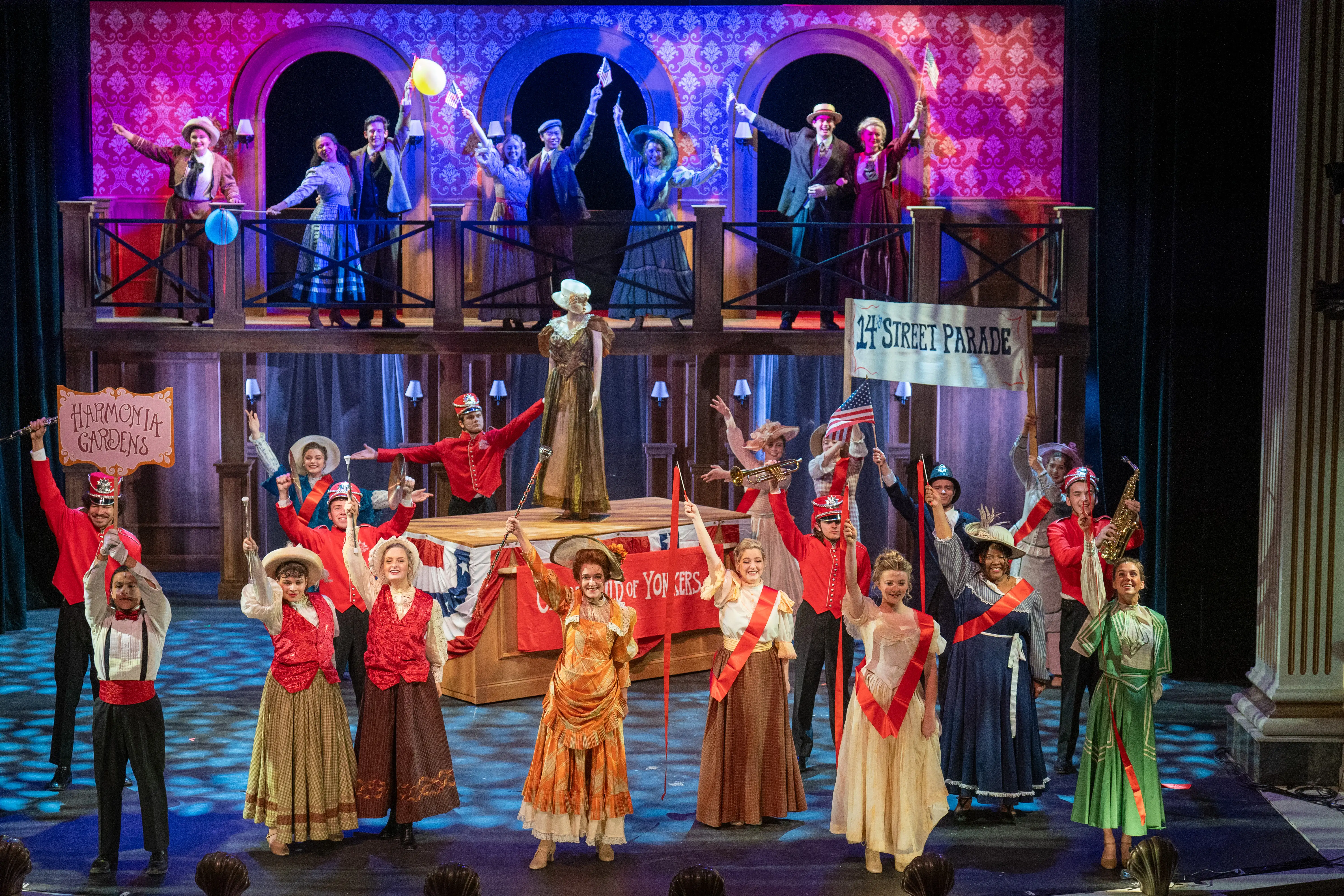 Colorful musical performance on stage at Troutt Theater featuring a large cast in period costumes holding signs and props in a vibrant set.