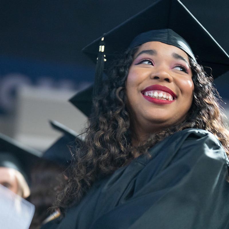 Graduate smiles to someone off camera while sitting in the Curb event center during graduation ceremony