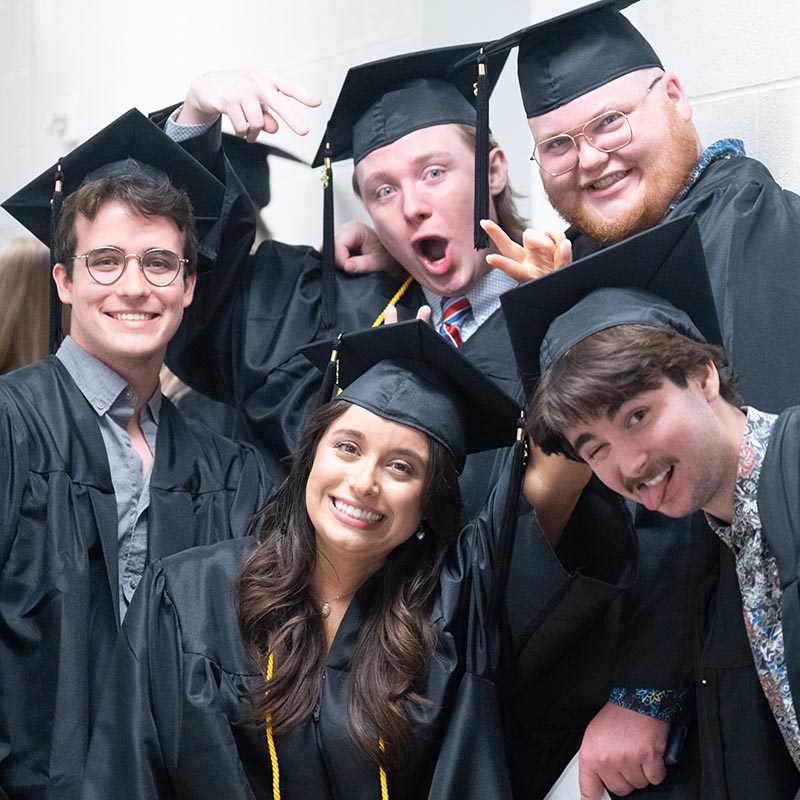 5 Graduates pose in hallway to Curb event center floor while lining for for graduation ceremony 