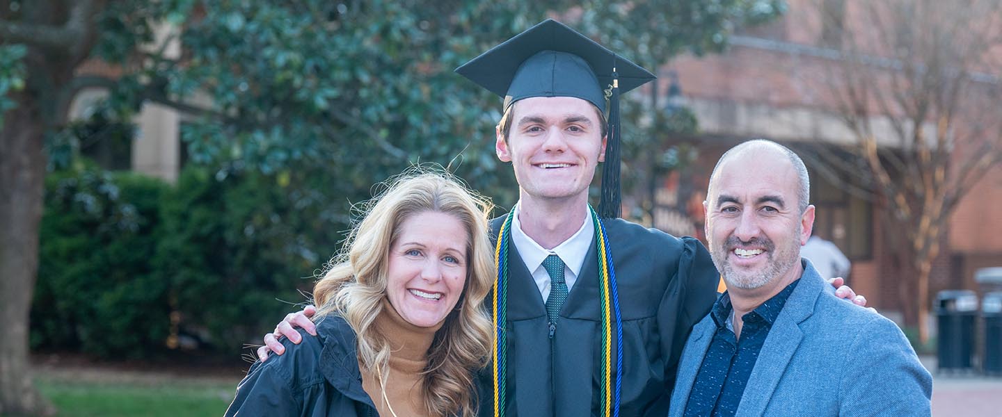 Graduate poses with his family for a picture outside before ceremony