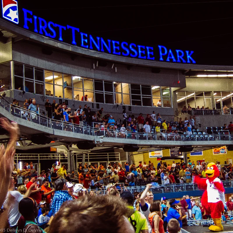 First Tennessee Park stadium at night with a red bird mascot entertaining a large crowd of fans during an event.