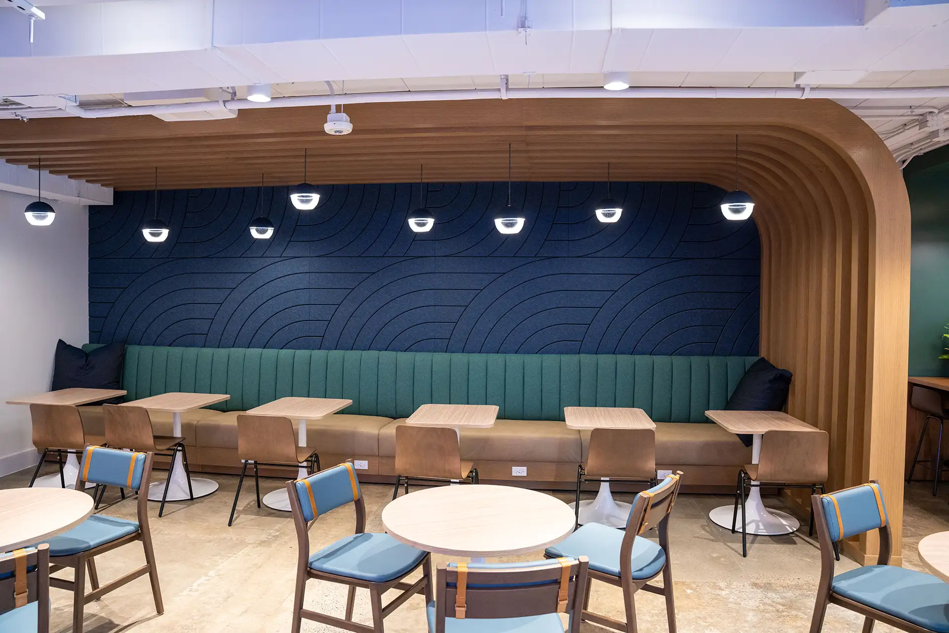 Dining nook with long green booth seating, wood tables, and modern pendant lighting under a wood-paneled ceiling.