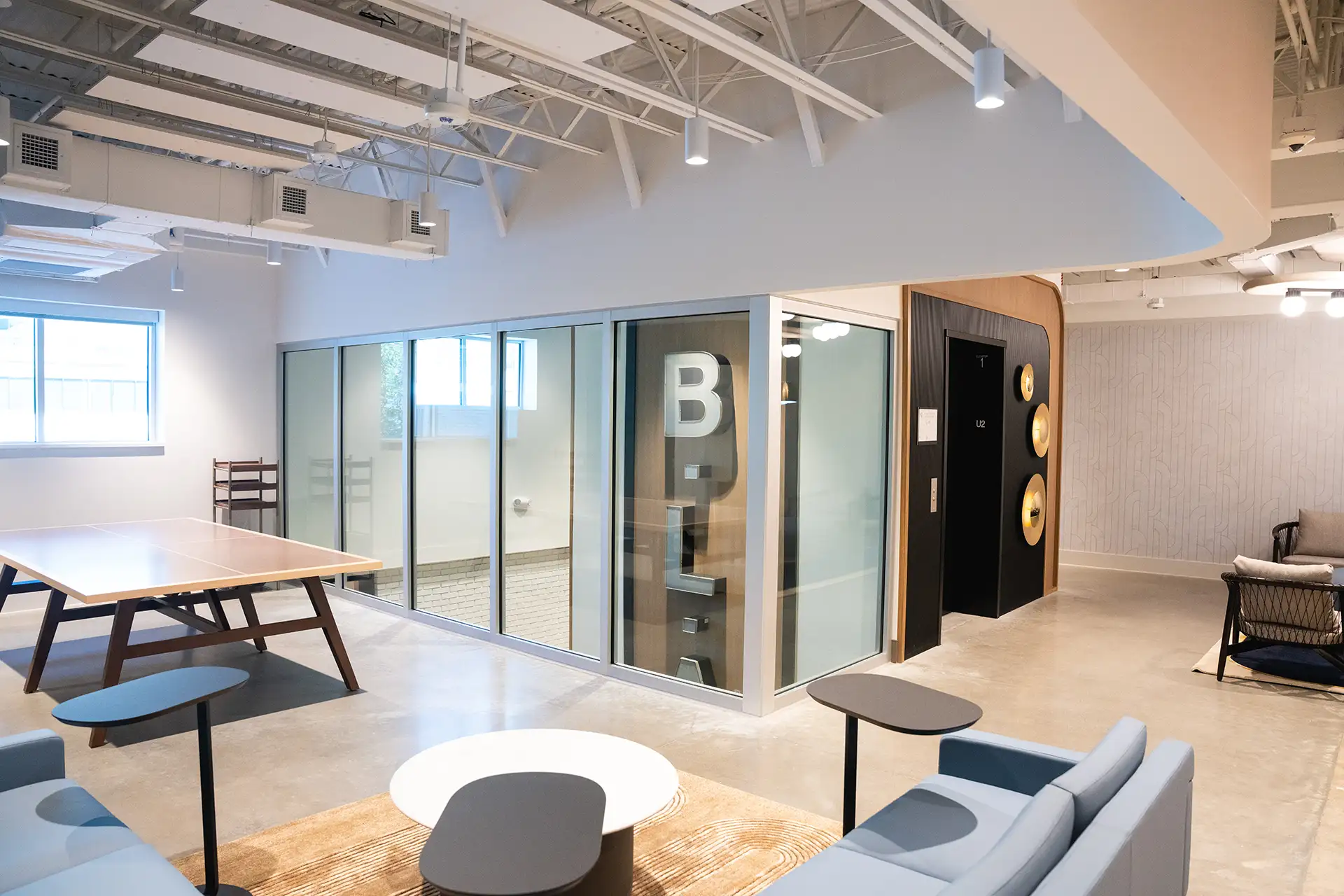 Recreation space featuring a ping pong table, lounge seating, and large “BLA” letters visible through glass walls.