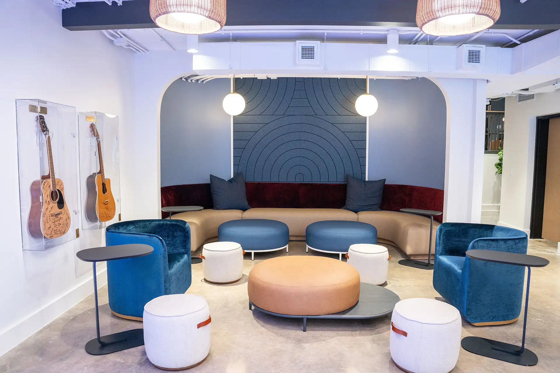 Seating area with blue velvet chairs, low tables, and guitars displayed in glass cases on the wall.