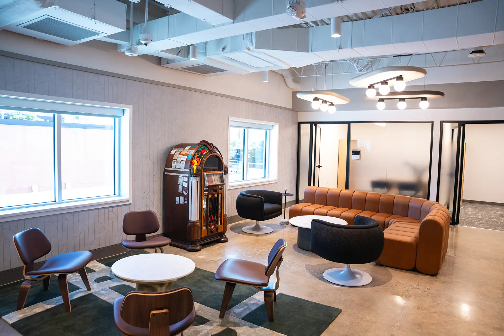 Lounge with modern chairs, round tables, a curved leather sofa, and a vintage jukebox in the corner.