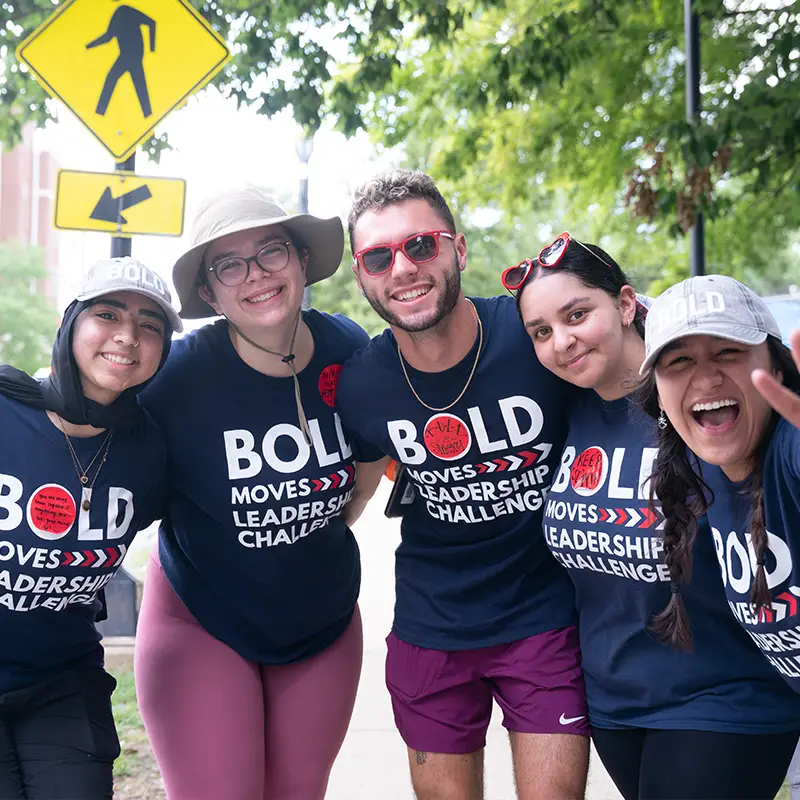 Five students embrace and smile at the camera wearing sunglasses and BOLD Moves teeshirts