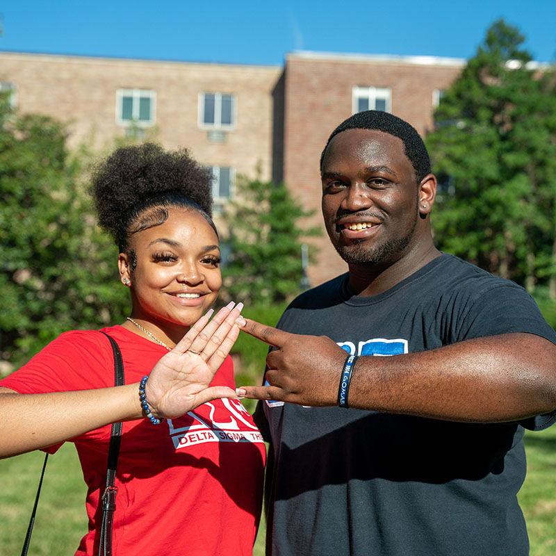 Two students sharing a hand sign at Greek Week
