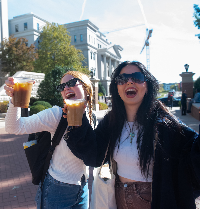 Two students holding up their coffees at It Must Be Wednesday