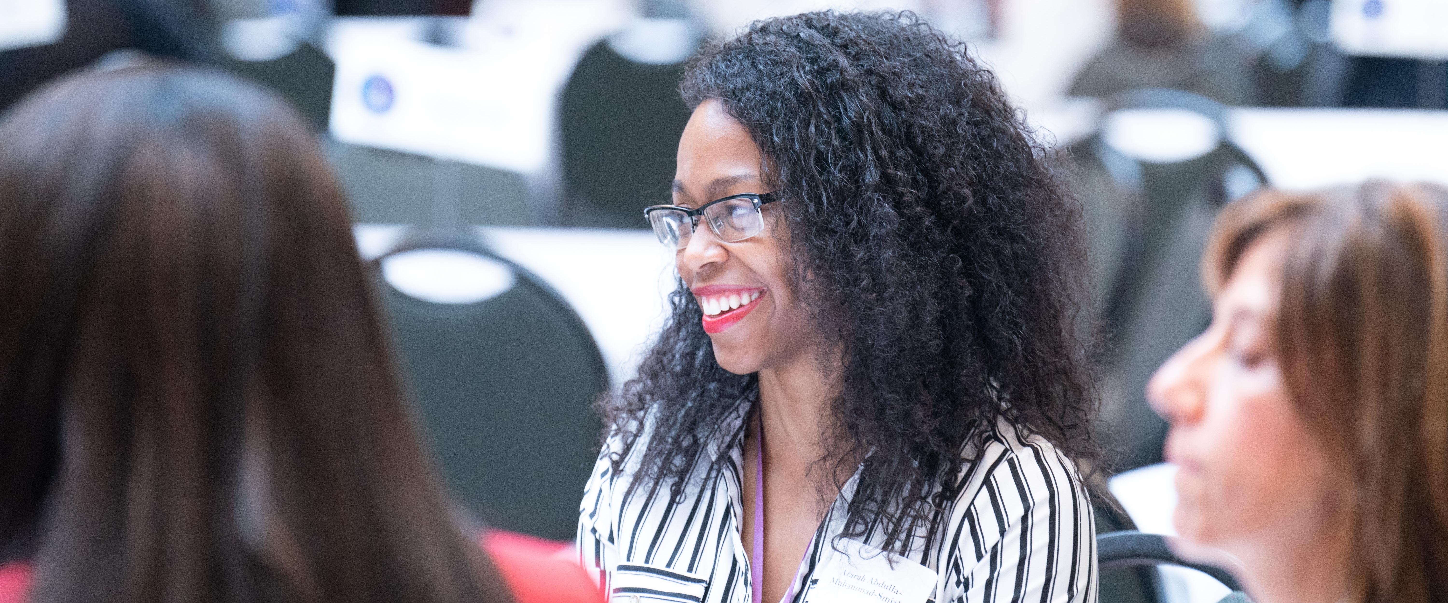 A woman smiling while sitting at a table of students during mentor program