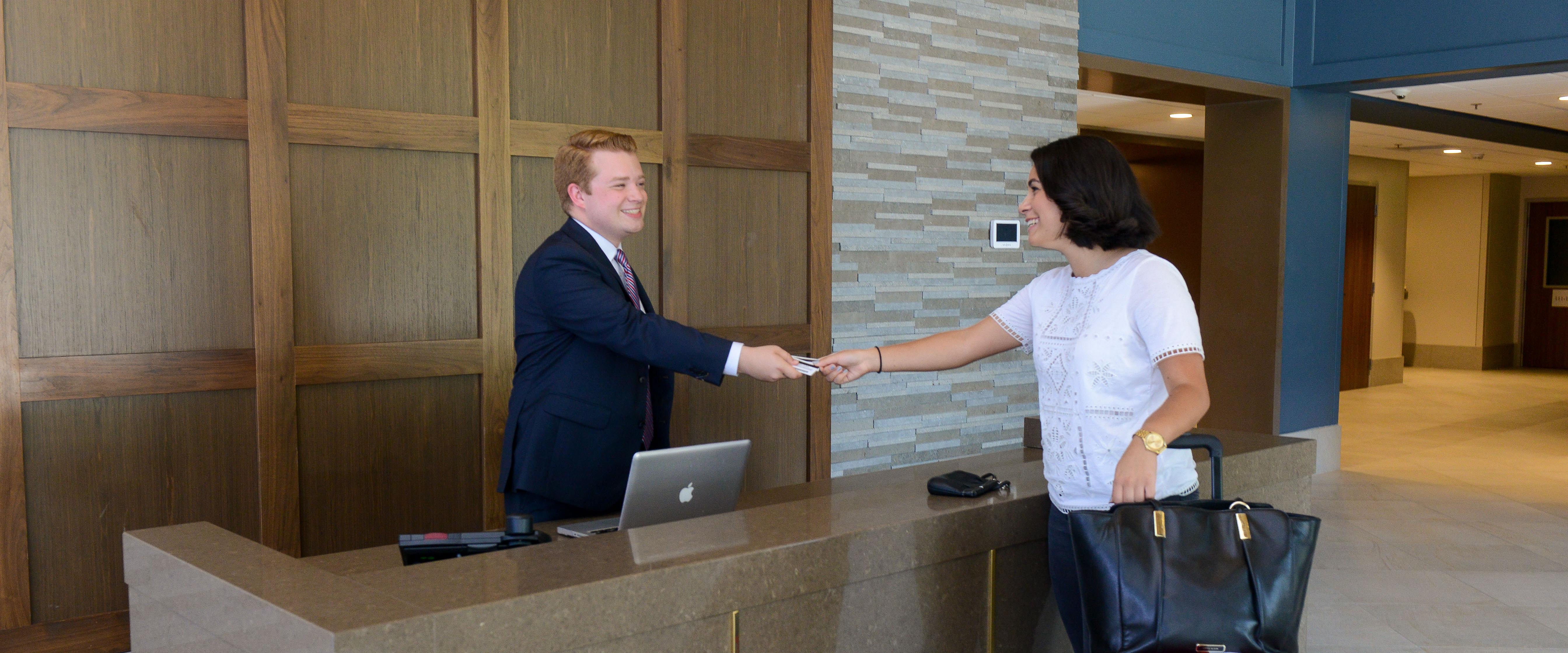 Women with suitcases receives room key cards from concierge behind a desk