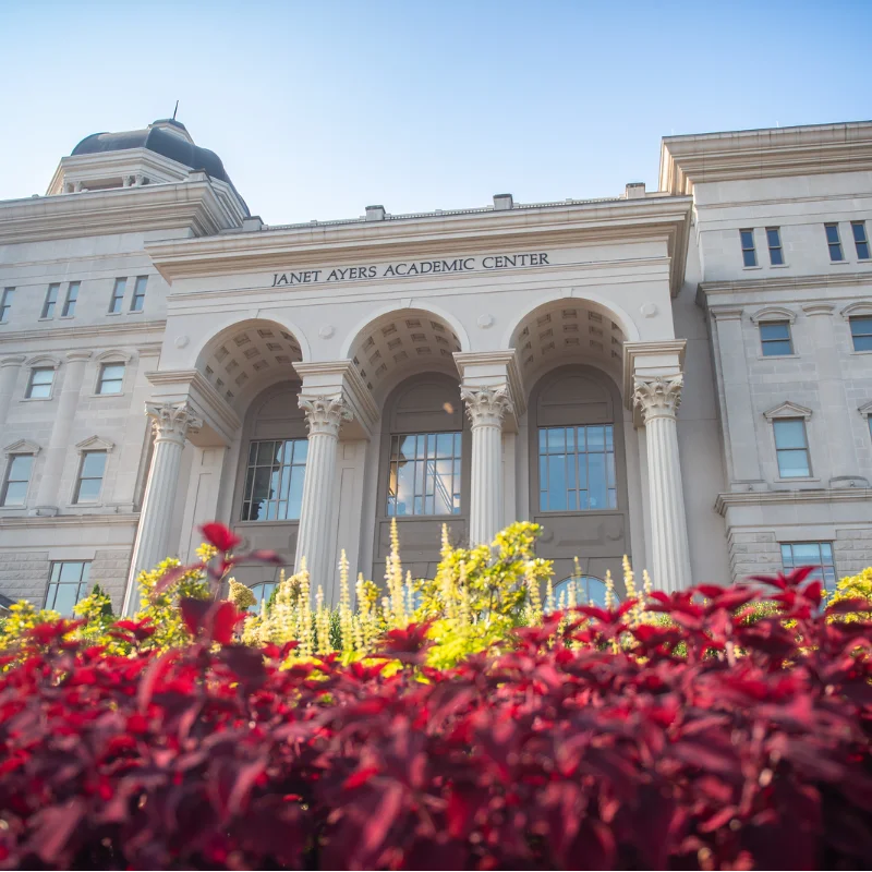 Janet Ayers Academic Center building with classical columns and arches, framed by vibrant red and yellow foliage.