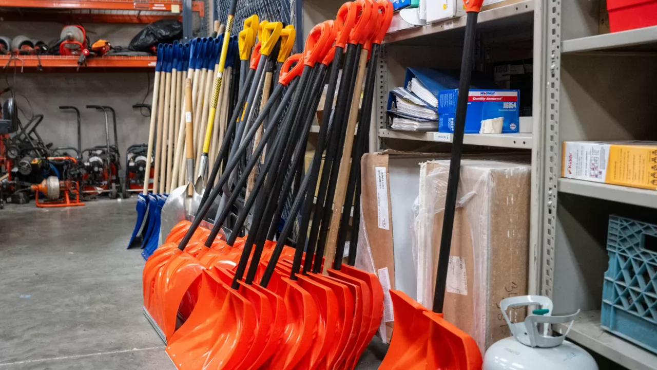 Large display of bright orange snow shovels with black handles in a retail or warehouse environment.